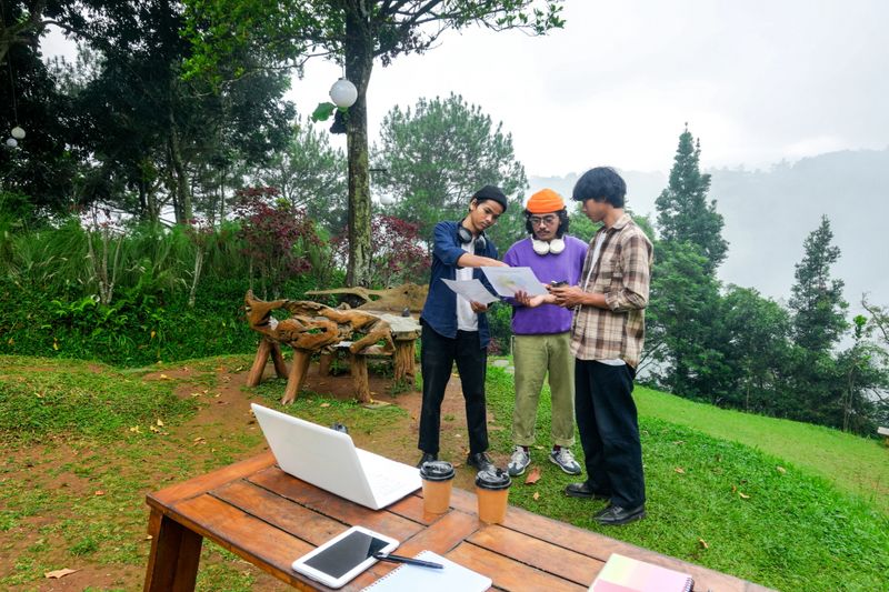 Young Entrepreneurs Collaborate on Project Outdoors Using Worksheet Amidst Lush Greenery