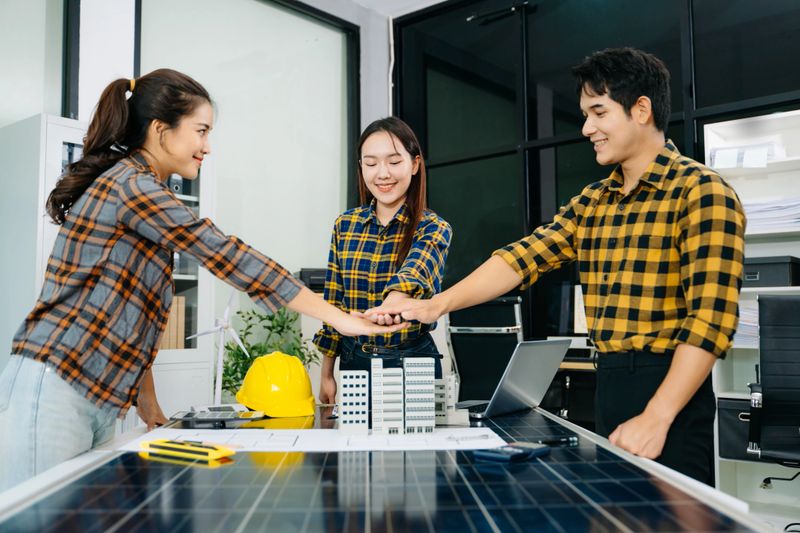 Professionals shake hands over solar panels and wind turbine models, symbolizing business success, teamwork, partnership, and sustainable innovation.