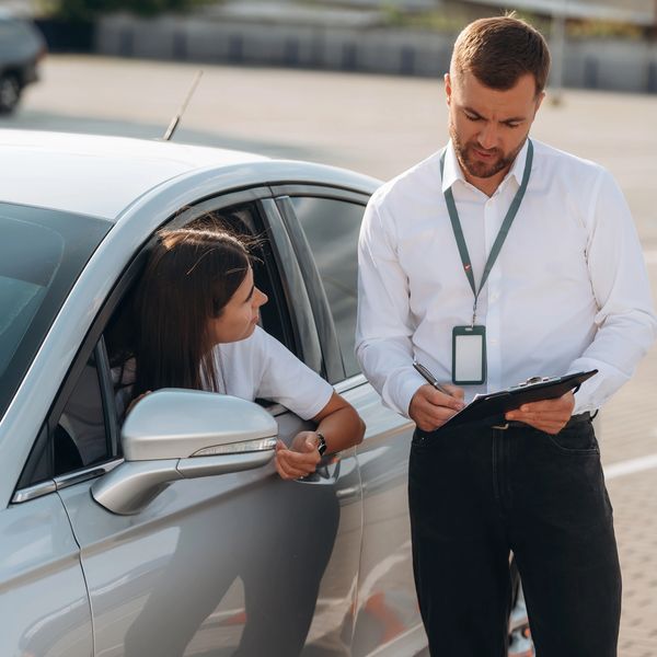 Woman talking to inspector next to her car.