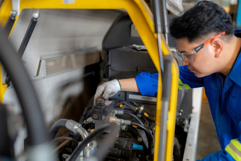 Engineer in safety gear and gloves examining engine performance in industrial workshop. Concept of maintenance, mechanical service, motor oil lubrication, safety control, repair work, and extending machine lifespan in the automotive industry.