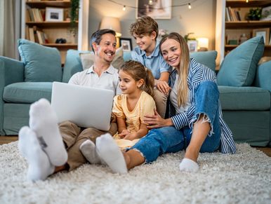 Happy family using laptop together on carpet.