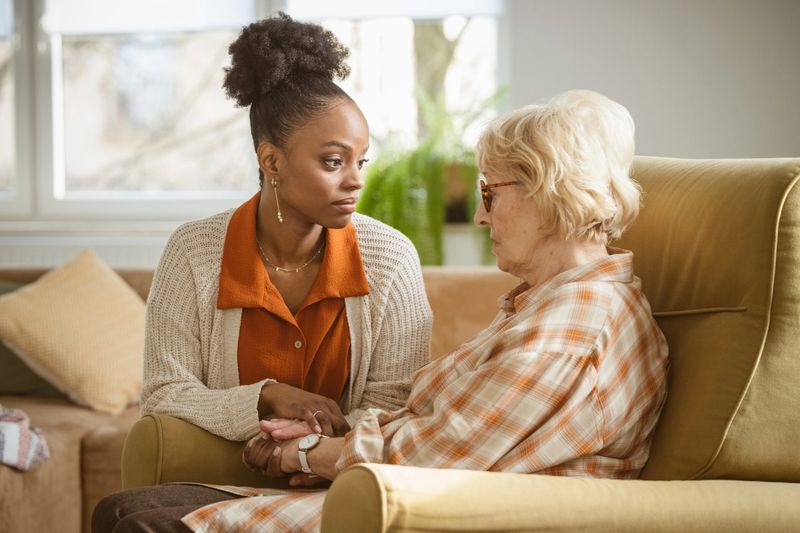 Smiling female home caregiver supporting senior woman in her house, talking with her. Senior lady holding walking cane.