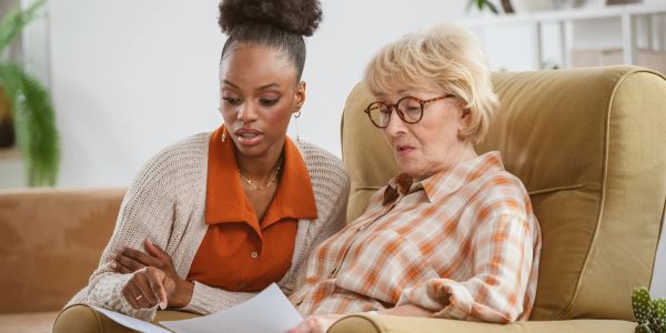 Young woman helps elderly woman with paperwork.