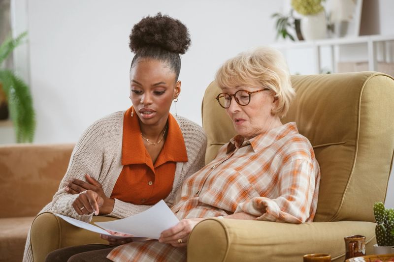 Female home caregiver supporting senior woman in her house, reviewing documents together.