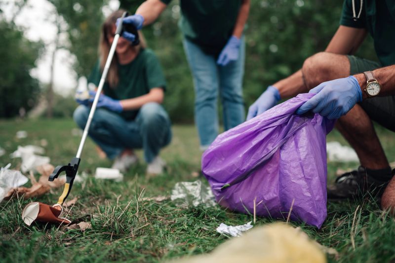 Group of volunteers actively working together, collecting discarded trash and waste from a green outdoor park