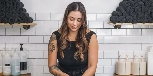 Woman with tattoos working in a spa or salon with rolled towels and bottles.