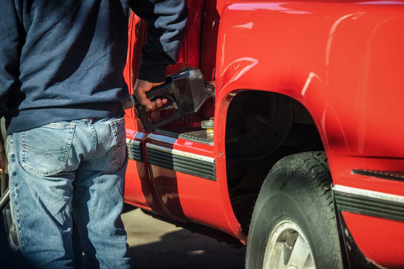 Man refueling red pickup truck at gas station in the United States. High quality photo
