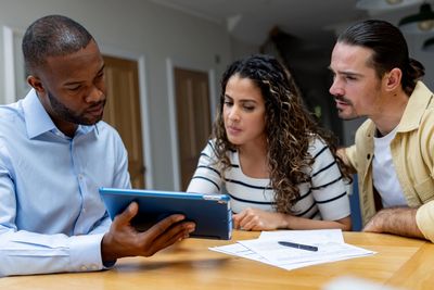 Three people discussing information on a tablet at a table.