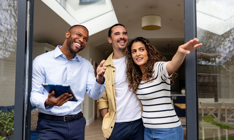 Happy real estate agent showing a couple the back yard of a house for sale through the sliding door