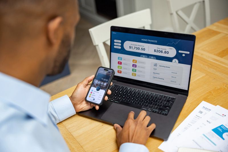 Close-up on a man at home looking at his bank statements using his laptop and cell phone - home finances concepts