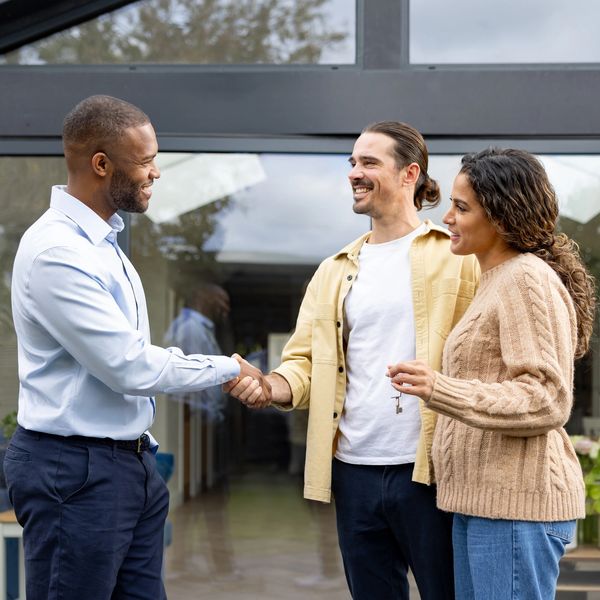 A man shaking hands with another man while a woman holds keys.