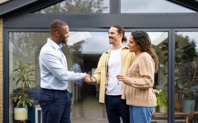 Two men shaking hands while a woman smiles nearby.