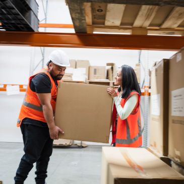 Two warehouse workers carrying a large box together.