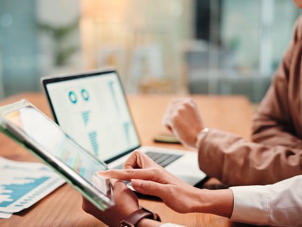 Two professionals analyzing data on a tablet and laptop in an office.