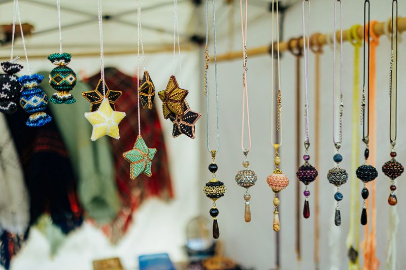 A colorful collection of handcrafted beaded necklaces and star-shaped ornaments hangs from a vendor's booth, showcasing artisanal detail and craftsmanship