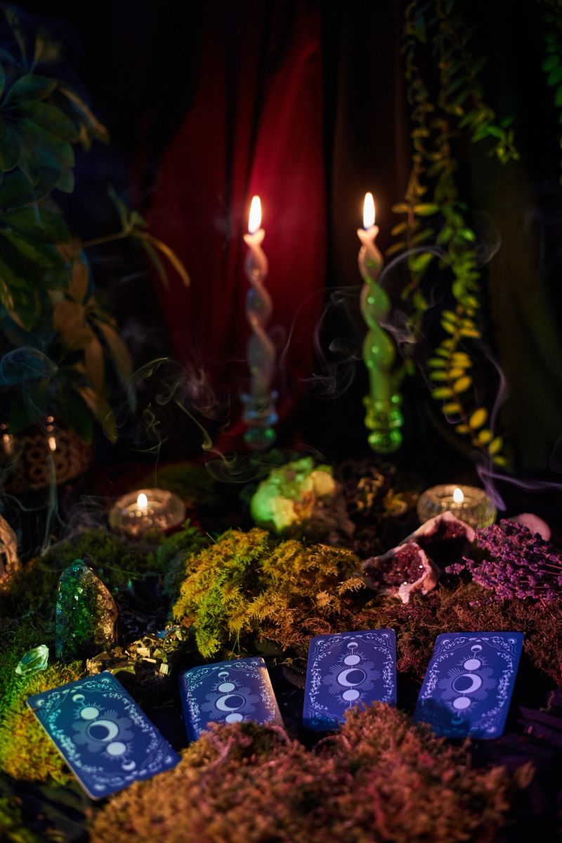 Tarot cards rest on a bed of moss, accompanied by flickering candles and plants, creating a serene atmosphere. soft light adds a magical touch to the scene.