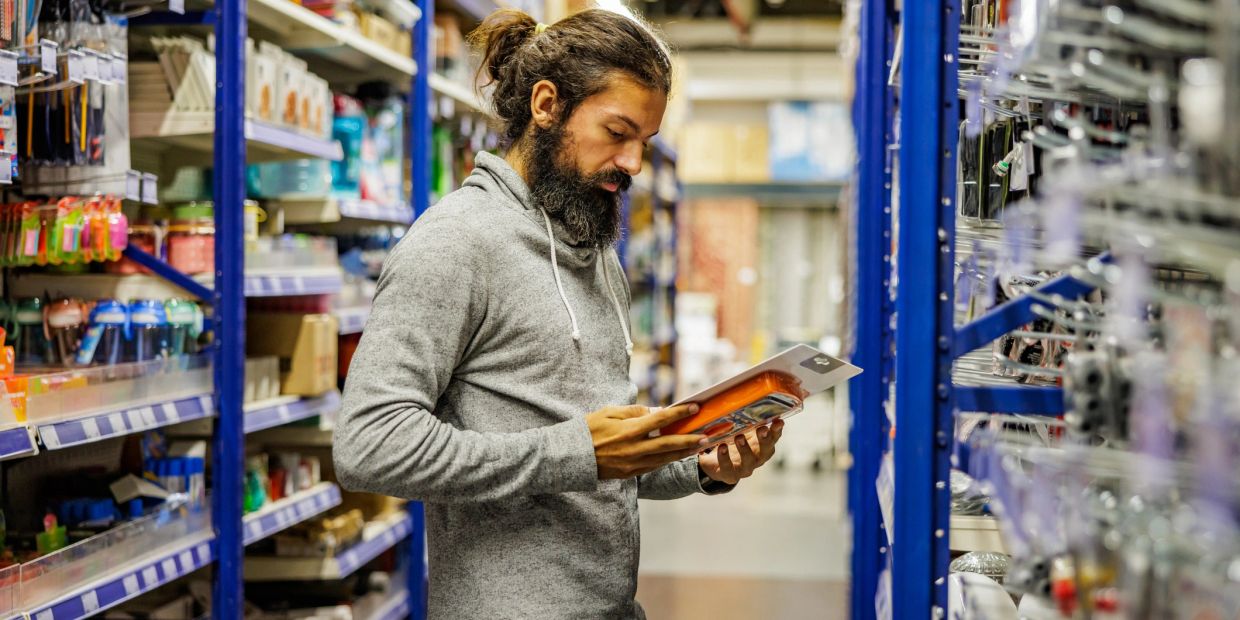 Man examining a packaged product in a store aisle.