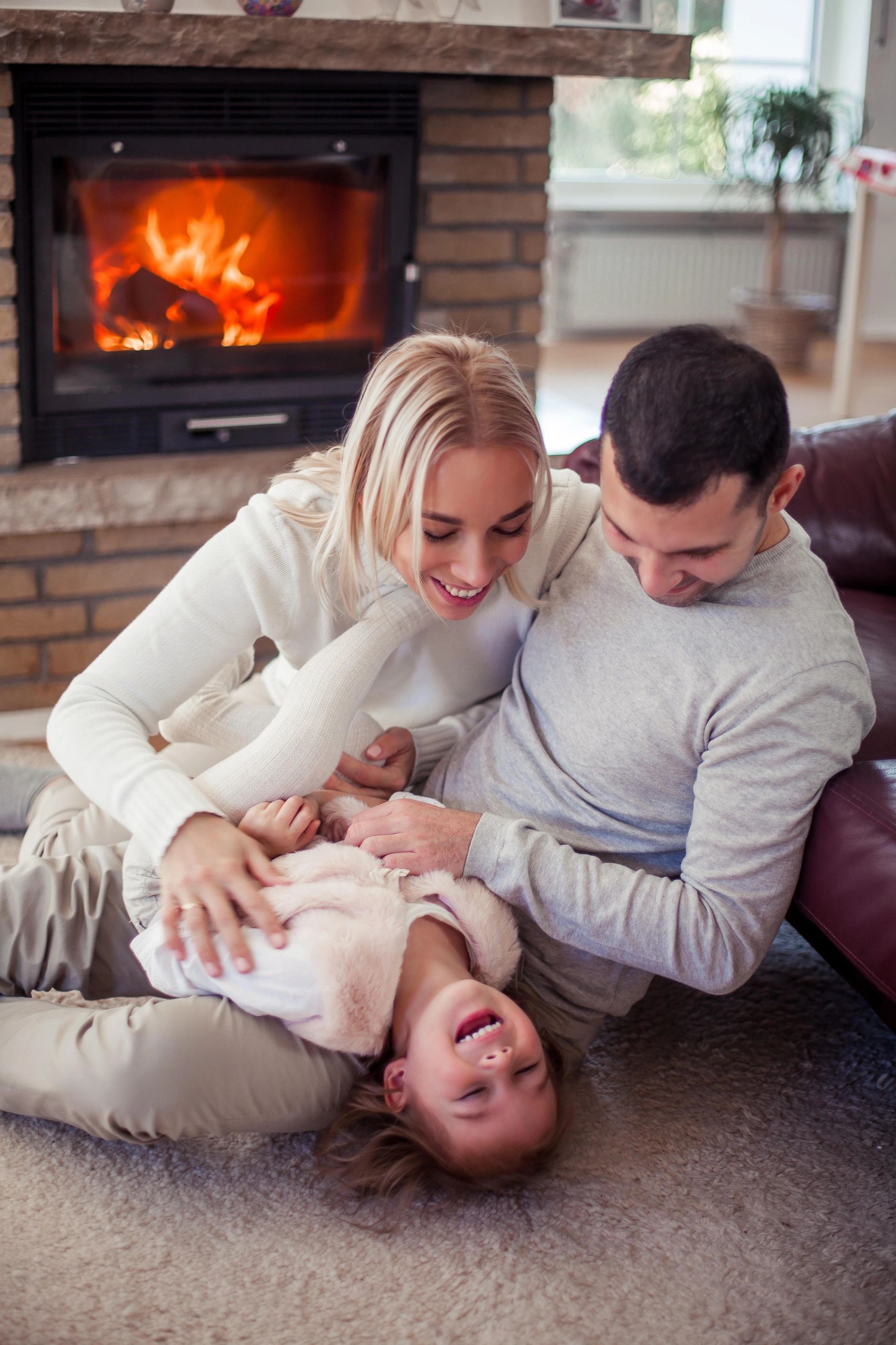 A man works on a laptop while a woman holds a baby in a cozy living room.