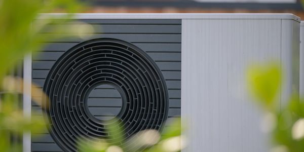 Close-up of an outdoor air conditioning unit with blurred greenery in the foreground.