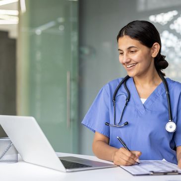 Nurse using laptop and taking notes with a smile.