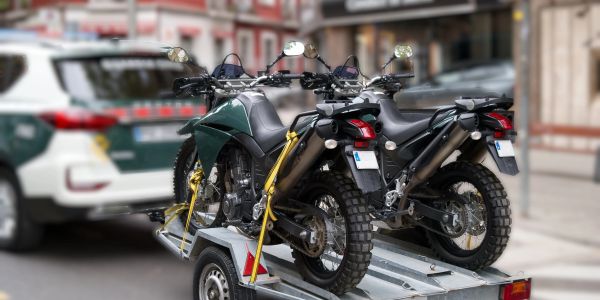 Two motorcycles are loaded on a trailer hitched to a police car.