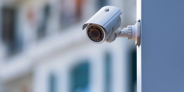 A white security camera mounted on a wall outdoors.