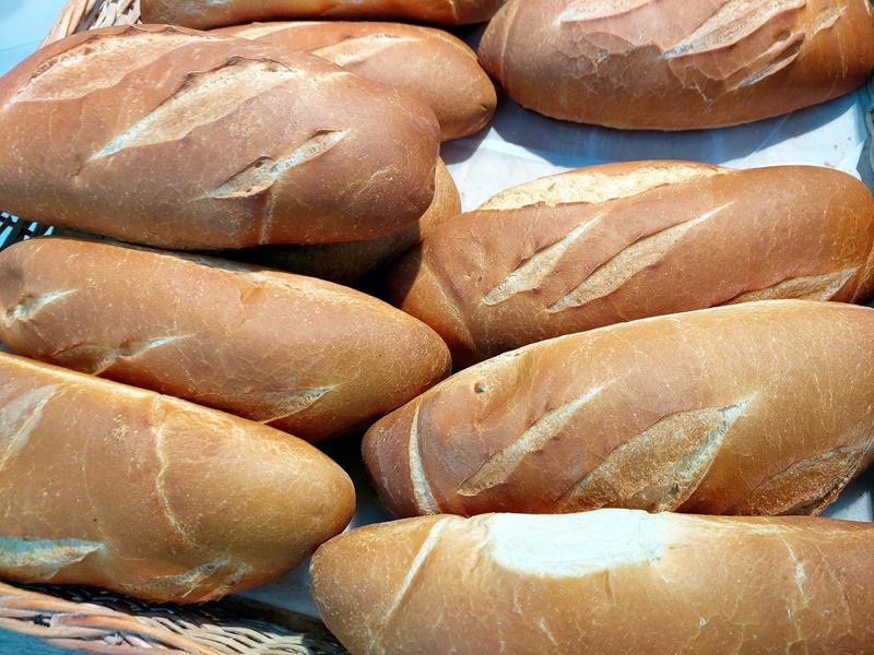 Warm wheat bread rolls sit invitingly in a woven basket, freshly baked and ready for breakfast at a local bakery during the early morning hours.