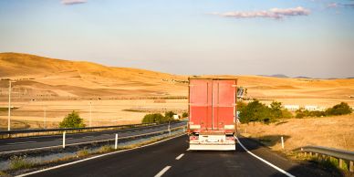 A red truck on an open highway through a dry landscape.