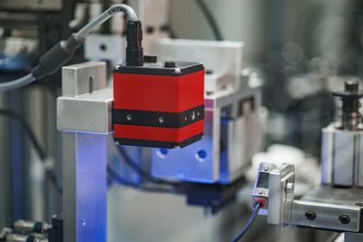Red industrial camera mounted on machinery for quality inspection.