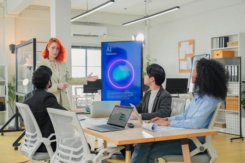 Diverse business professionals male and female meet in bright office interior, using AI virtual assistant to brainstorm, connect big data dots, discuss creative strategy teamwork growth and progress