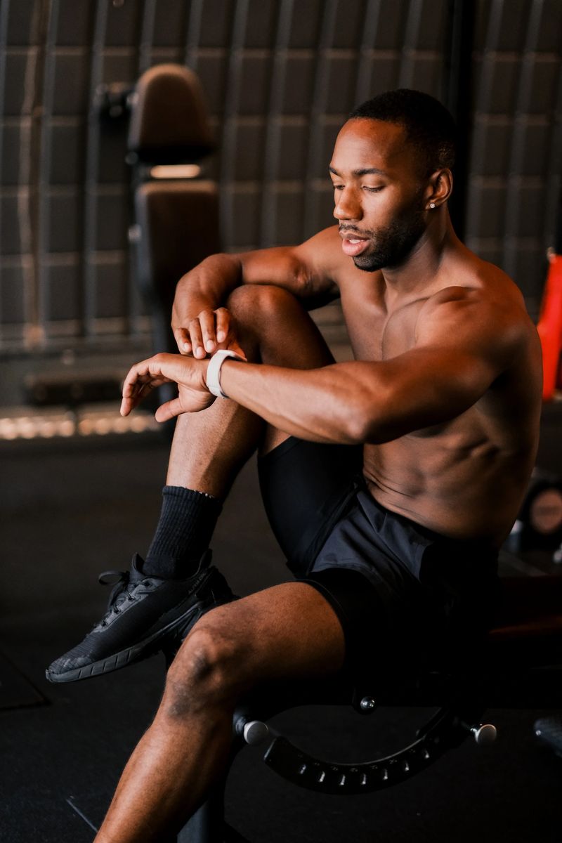 A fit Black athlete stretching his arms during a workout in a gym. Smiling male fitness trainer warming up, showing strength, health, and active lifestyle. Keywords: fitness, gym, stretching, athlete, workout, warm-up, trainer, active lifestyle, strong male model.