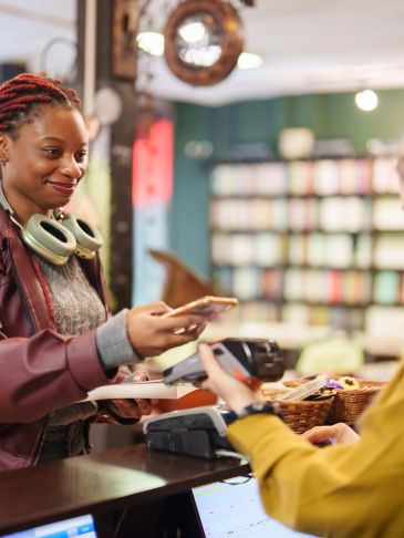A woman makes a contactless payment at a store counter with a smile.