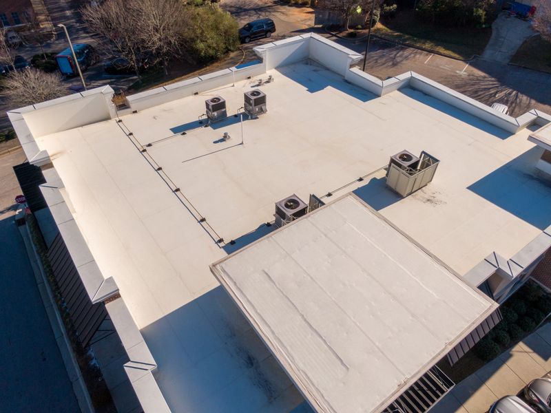 Drone aerial images showing a variety of commercial and industrial buildings with white TPO flat roofing systems. The photos highlight clean reflective roof membranes, rooftop HVAC units, and detailed architectural layouts under bright daylight. These images illustrate modern energy-efficient roofing materials used in urban and suburban commercial developments.