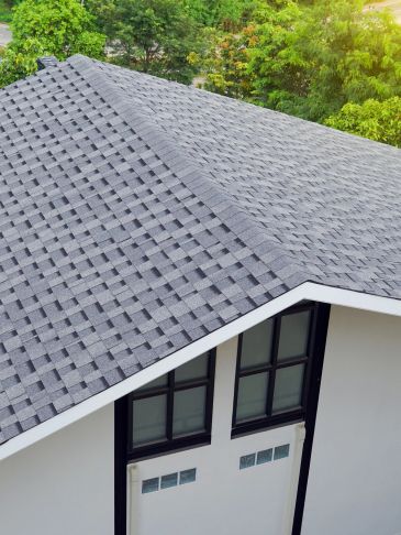 Modern house roof with patterned gray shingles and surrounding greenery.