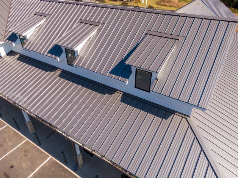 Drone aerial photos showcasing commercial buildings with sleek standing seam metal roofs. The images highlight the reflective steel panels, clean architectural lines, and durable construction used in contemporary retail and industrial facilities. Captured under bright sunlight, emphasizing the modern design and energy efficiency of metal roofing systems.