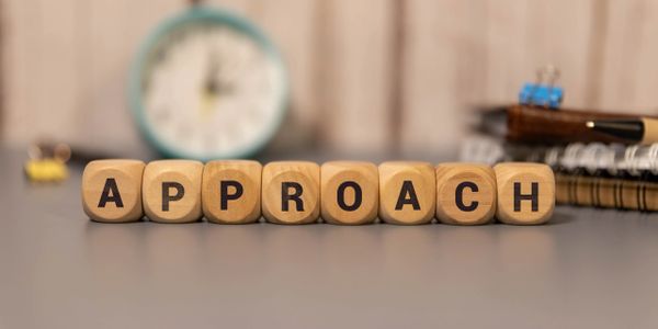Wooden blocks spell out the word APPROACH on a desk with blurred background.