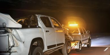 Tow truck pulling damaged white pickup truck at night.