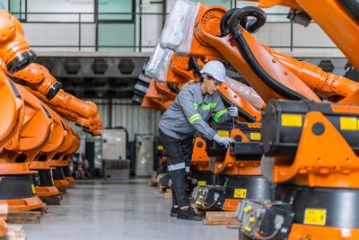 Worker inspecting robotic arms in a factory.