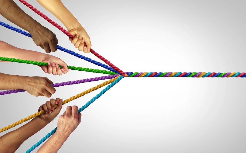 United And Pulling Together as a motivational team building concept with a group representing unity joining as one to combine thier individual strengths for collective success as hands that pull different ropes creating a unified force to succeed.