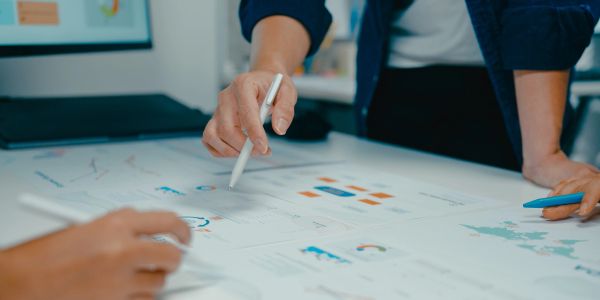 Person pointing at charts on a table with a pen.