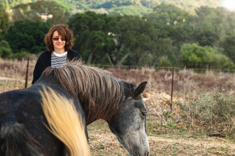Woman in front of a horse during an equine therapy session in the countryside. Concept of emotional health, animal connection, well-being, and personal development.