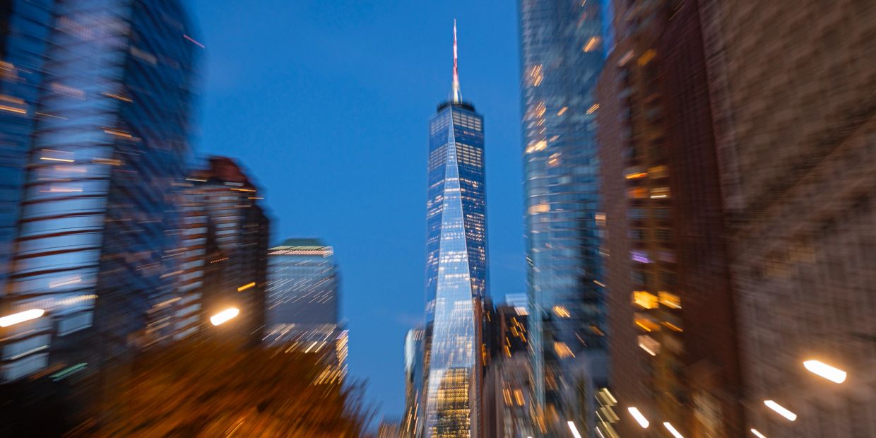 Blurred city skyline at dusk with a tall skyscraper.
