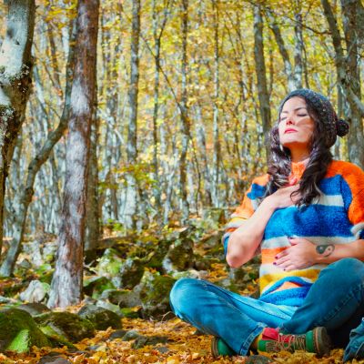 Woman meditating in a colorful sweater in a forest.