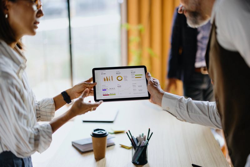 Business colleagues analyzing financial charts and graphs on a tablet screen during a meeting, discussing market trends