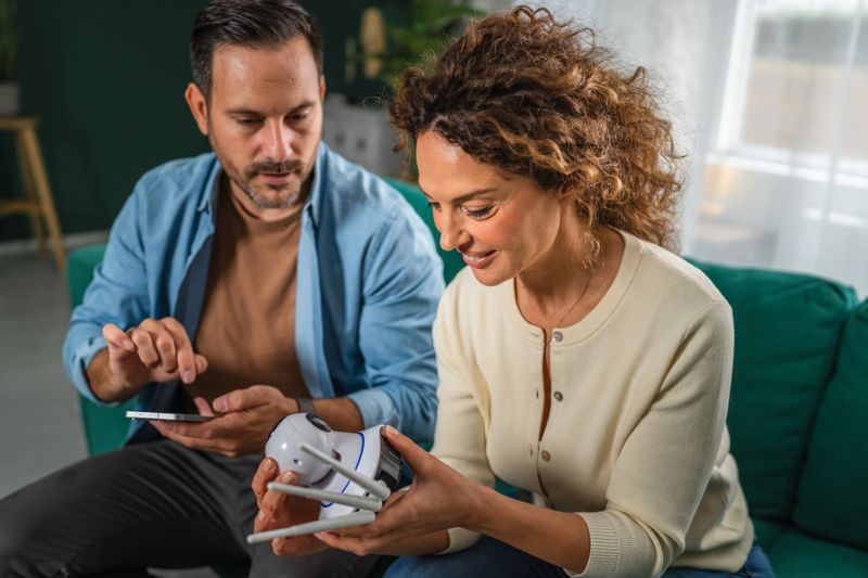 Couple installing and configuring a new smart home security camera, with the man operating a smart phone for setup while the woman holds the device, highlighting modern technology and protecting home