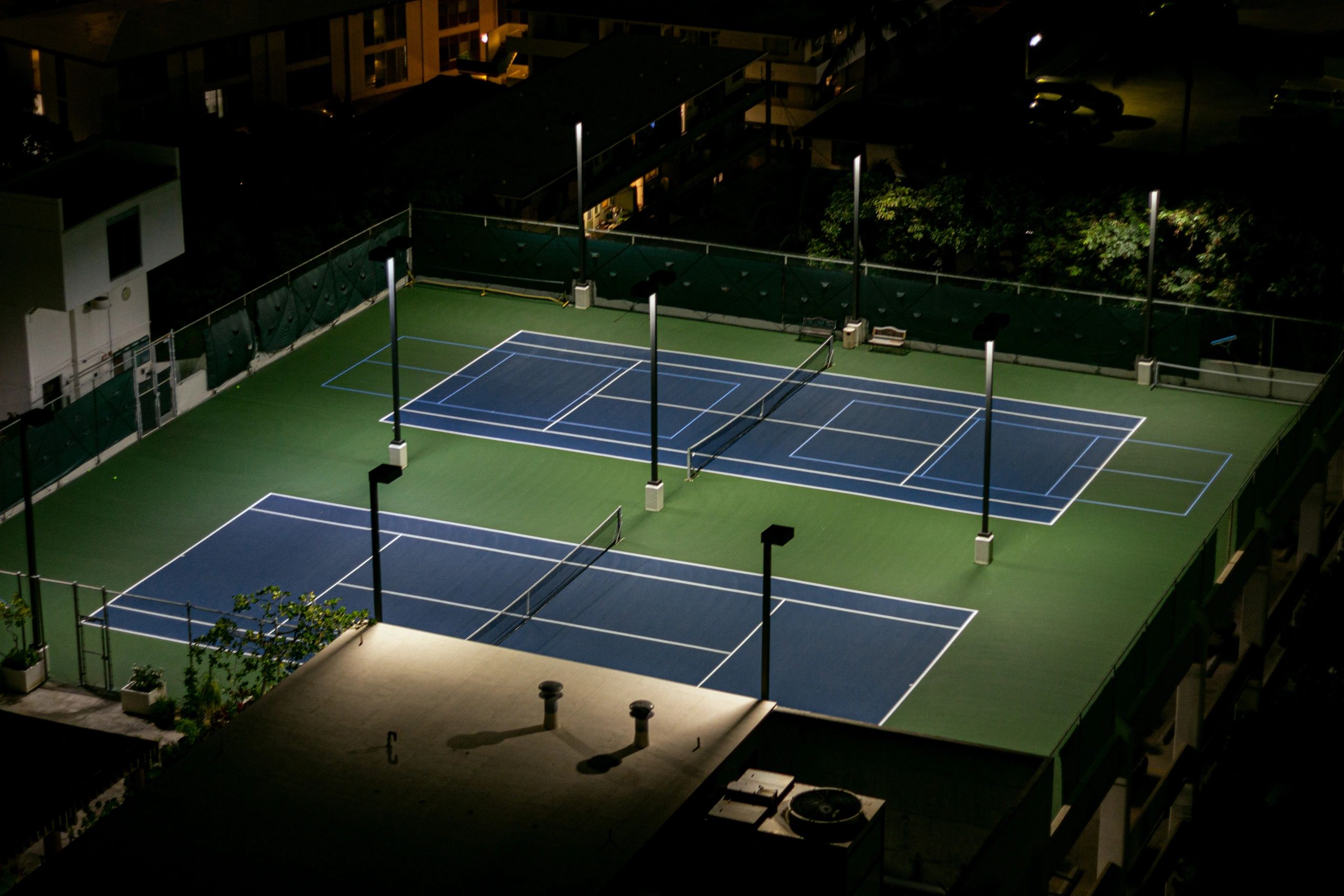 Empty illuminated tennis courts at night.