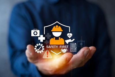 Hand holding safety first icons with a worker helmet.