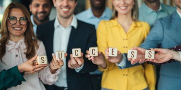 A diverse group of professionals holding blocks spelling SUCCESS with smiles.