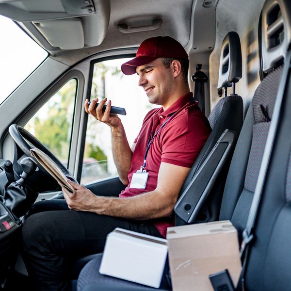 Delivery driver using phone inside van with packages nearby.