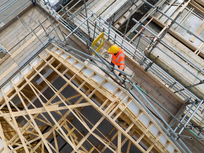 Construction worker on building site showing housebuilding,roof trusses, scaffolding and completed houses. Cornwall, UK
